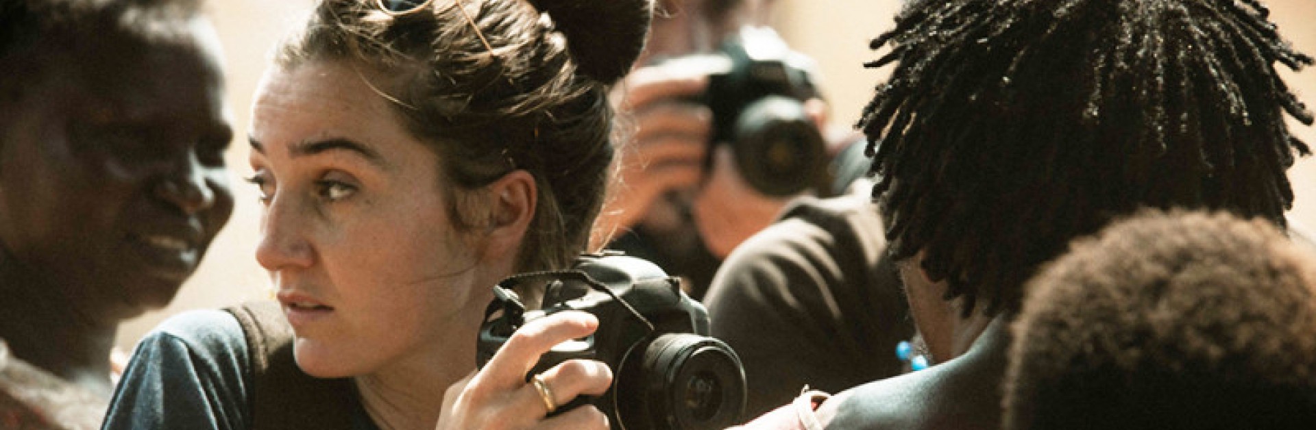 Une foule de personne, dont une femme avec un appareil photo qui regarde vers la droite