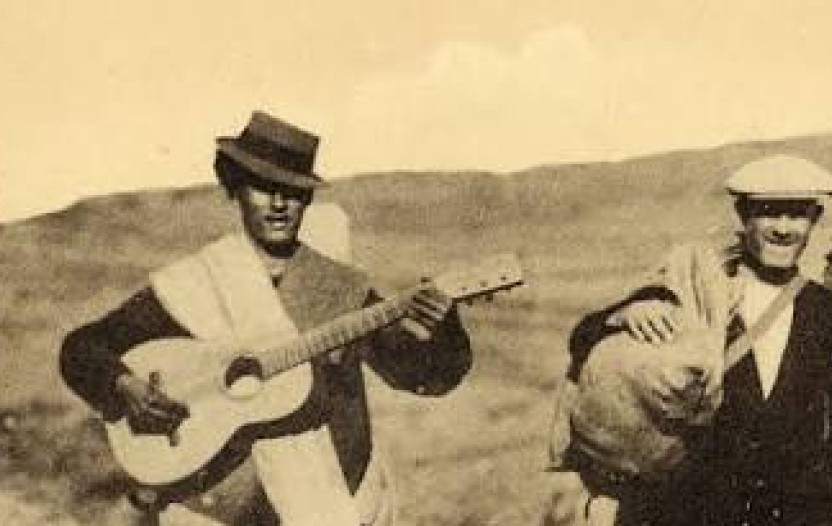 4 hommes marchent. L'un porte une guitare, les 3 autres des sacs. C'est une photographie assez ancienne des années 40.